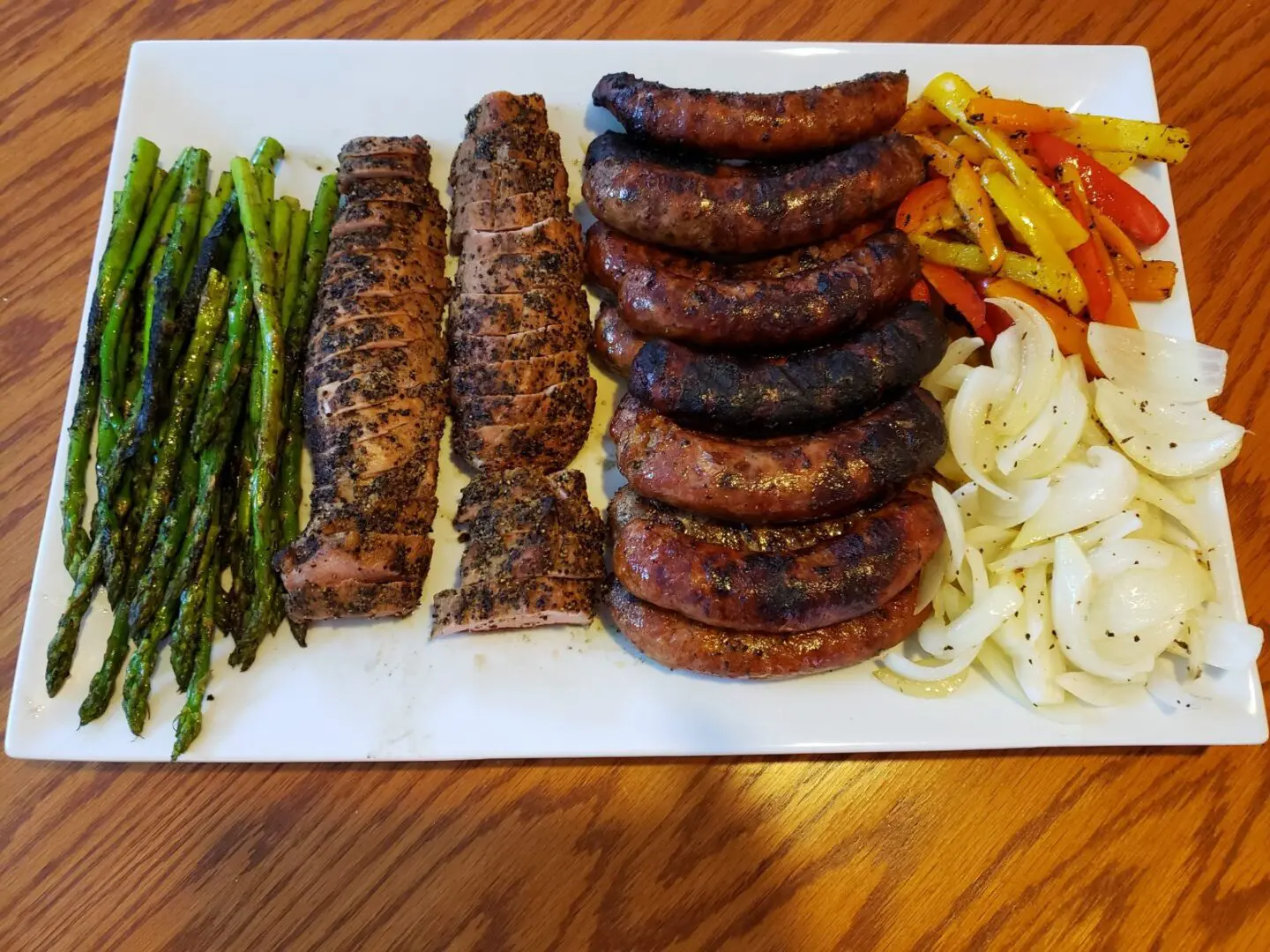 A plate of food with asparagus, onions and sausage.